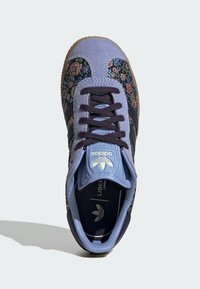 Sneaker blu in suede con motivo floreale in vari colori, suola in gomma e lacci neri. Il marchio è visibile sulla linguetta.