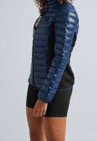 Laivastonsininen toppatakki, jossa vaakasuora tikattu kuvio, mustat sivupaneelit ja korkea kaulus. Varustettu koko pituuden vetoketjulla ja logoyksityiskohdalla nauhassa.