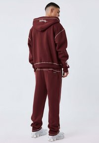 Conjunto de sudadera y pantalones de chándal burdeos, hecho de un tejido suave, con costuras en contraste, capucha y bolsillos laterales. Detalles en blanco.