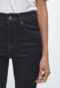 Tmavě modré džínové kalhoty s vysokým pasem, s předními kapsami, stříbrným zapínáním na knoflík a kontrastními švy. Hladká textura, těsně přiléhající střih.