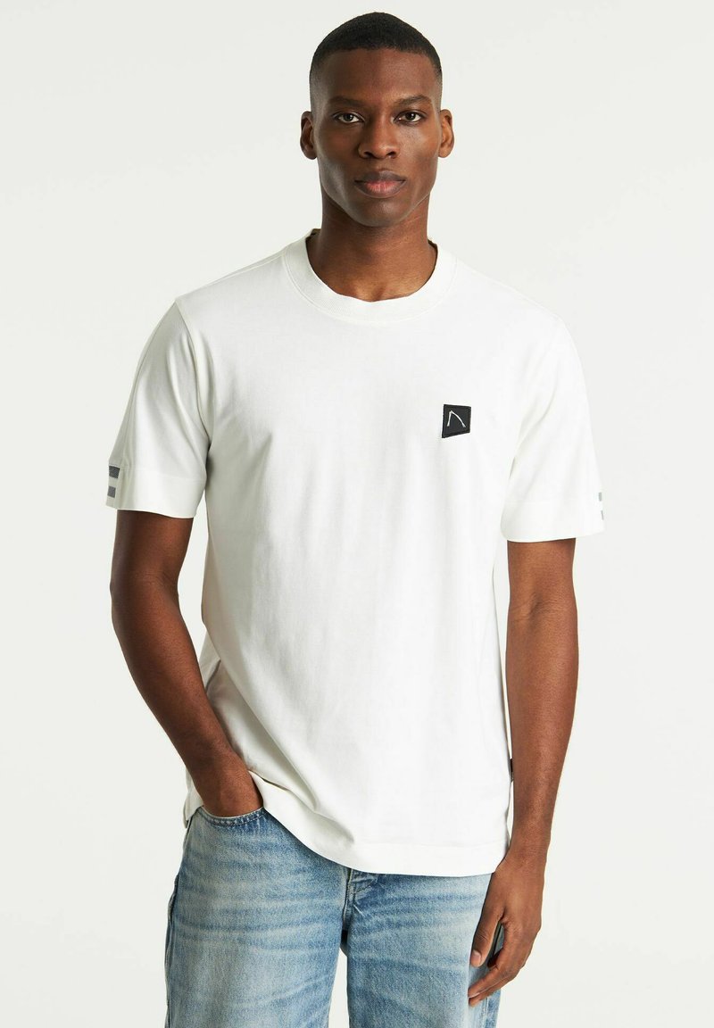 T-shirt bianco a maniche corte realizzato in cotone. Presenta un piccolo logo quadrato nero sul petto e un accento a strisce grigie sulle maniche.