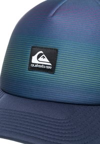 Gorra de béisbol con rayas degradadas en tonos azul-verde, fabricada en un tejido suave, con visera curvada y parche del logo negro de Quiksilver en la parte frontal. Acabado texturizado en la visera.