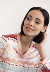 Multicolored blouse with floral and wavy patterns, featuring a V-neck, contrasting trim, and decorative buttons on the cuffs. Smooth fabric.
