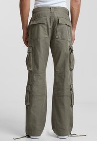 Pantaloni cargo de culoare verde măslinie, cu o croială lejeră, multiple buzunare laterale și manșete elasticizate. Fabricati dintr-un material durabil, cu o textură netedă.