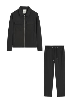 Veste noire zippée avec deux poches avant à rabat, associée à un pantalon noir à cordon de serrage.