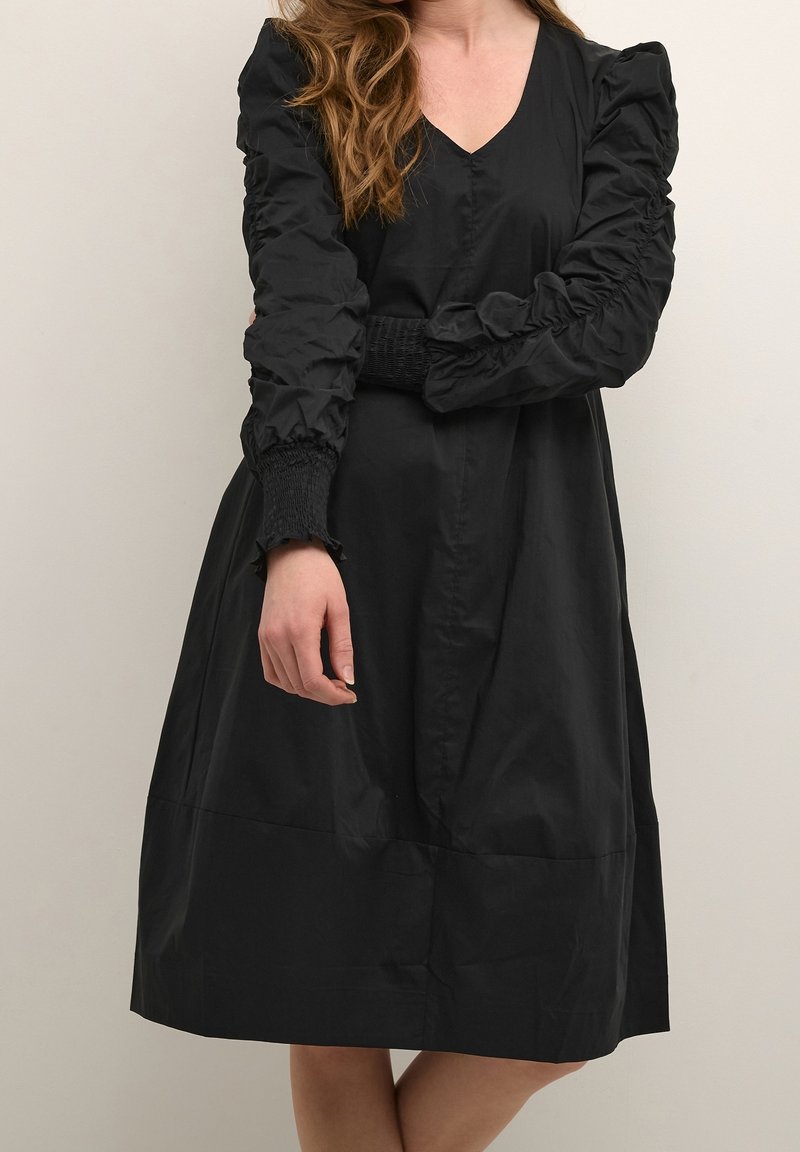 Vestido negro con escote en V, que presenta mangas abullonadas y puños fruncidos. Confeccionado en un material suave y liviano con un corte relajado.