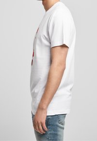 Wit katoenen T-shirt met korte mouwen, voorzien van een kleurrijk grafisch ontwerp aan de voorkant. Draagt blauw spijkerbroek.