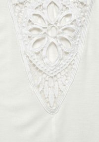 Witte stof met ingewikkelde kantdetails en een bloemmotief in het midden. Glad van textuur, delicate uitsparingen en golvende randen.