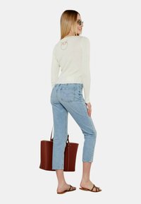 Maglione a coste di colore crema chiaro con logo sul retro, abbinato a jeans cropped azzurri, borsa a tracolla marrone e sandali piatti marroni.