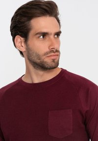 Bordeaux pitkähihaista paitaa, jossa on ribbitekstuuri, pyöreä kaula-aukko ja vasemmalla rintatasku; sisältää raglan-hihoja mukavuutta varten.