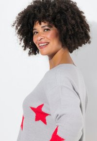 Maglione grigio a maglia con grandi motivi a stella rossa. Il design ha una vestibilità comoda con un colletto ampio e una texture morbida.