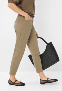 Un pantalon kaki ajusté avec une poche latérale, associé à des ballerines en mesh noires et à un sac fourre-tout texturé noir. Tissu lisse avec un léger éclat.