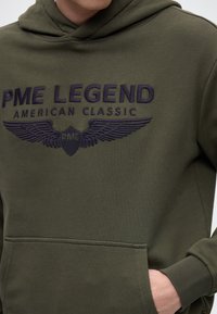 Bluza z kapturem w kolorze oliwkowej zieleni z haftowanym napisem "PME LEGEND AMERICAN CLASSIC" oraz wzorem skrzydeł, posiadająca przednią kieszeń i ściągacze na mankietach.
