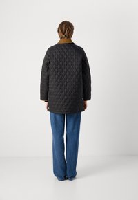Quilted black jacket with a brown corduroy collar, featuring a loose fit and gold hardware details, worn with blue wide-leg jeans.