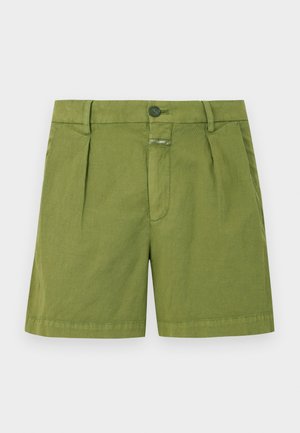 Haut blanc à manches longues avec boutons, short vert taille haute, et bottines marron. Design simple avec une coupe décontractée.