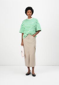 T-shirt oversize rayé vert et blanc à manches courtes, associé à une jupe beige arrivant au genou avec des poches sur les côtés, et des ballerines noires.