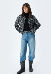 Giacca leopardata in nero e grigio, dolcevita nero, jeans azzurri chiari e stivali da cowboy neri con cuciture decorative.