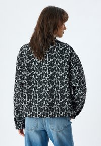 Giacca oversize con stampa leopardata nera e grigia, con maniche lunghe e orlo arrotondato, abbinata a jeans in denim blu chiaro.