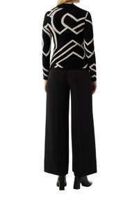 Schwarzer Strickpullover mit kontrastierendem cremefarbenem abstraktem Muster, kombiniert mit hochtaillierten, weiten Hosen. Glatte Textur und taillierter Schnitt.