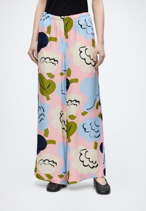 Pantalones de pierna ancha con fondo rosa y grandes patrones florales azules, blancos y verdes, combinados con zapatos negros y una parte superior negra.