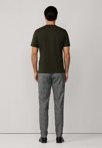 Camiseta de algodón verde oliva combinada con pantalones grises de cuadros. Los pantalones presentan un patrón texturizado. El modelo está de espaldas a la cámara.
