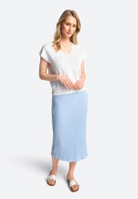 Lichtgrijze, korte mouwen top, V-hals; blauwe, gestructueerde midi rok met golvend patroon; witte slidesandalen met verstelbare riem.