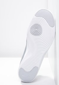 Sole di sneaker con una parte inferiore in gomma bianca liscia e modelli di battistrada circolari e ondulati; accenti grigi sui lati.