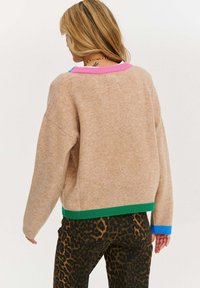 Beżowy sweter o luźnym kroju, z zielonymi, różowymi i niebieskimi prążkowanymi akcentami na kołnierzu i hemie. Teksturowany, miękki materiał.