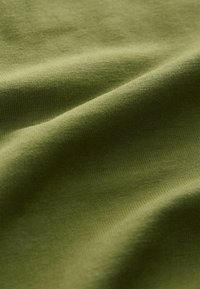 Oliivivihreä puuvillakangas, jossa on pehmeä ja sileä pinta, esittää helliä laskoksia ja tasaisesti kudottua kuviota kauttaaltaan.