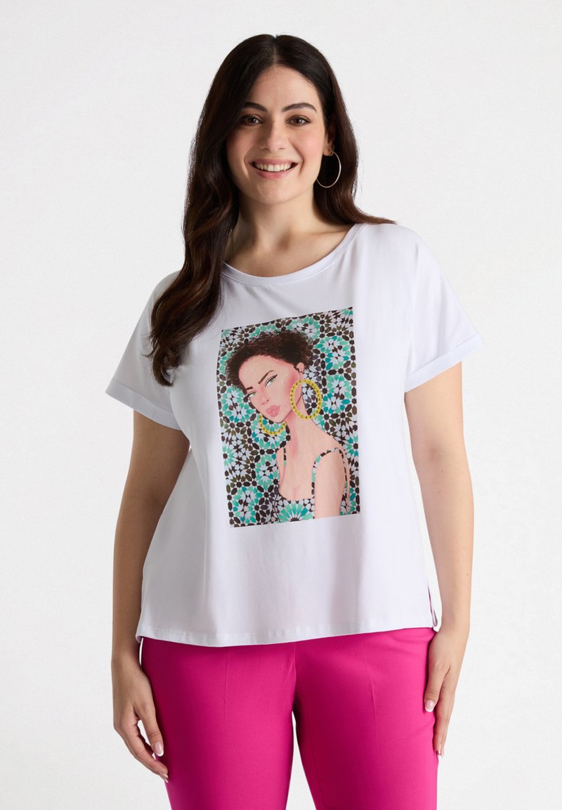 Hvid T-shirt med korte ærmer, der har et farverigt grafisk print af en kvinde, med blomsterprint og udsmykninger, parret med lyserøde bukser.