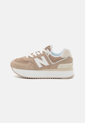 Beige og hvid New Balance-sneaker med overdel i ruskind og mesh, hvide snørebånd, tyk sål og "N"-logo på siden, vist fra ydersiden.