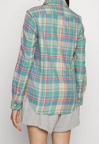 Rutig skjorta med en blandning av gröna, blå, röda och krämfärgade nyanser, med rundad nederkant, knäppta ärmar och klassisk krage.