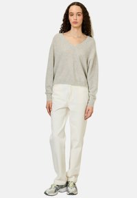Pull en V gris en matériau doux, associé à un jean droit blanc et des baskets de sport multicolores.