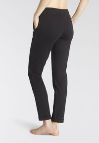 Schwarze Sweatpants mit elastischem Bund, seitlichen Taschen, schmal zulaufendem Design und umgeschlagenen Säumen, hergestellt aus softem, elastischem Material.