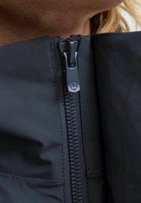 Zwarte jas met een close-up van een rits, voorzien van een matte afwerking en textuurrijk stof, met nadruk op het stiksel en het detail van de ritssluiting.