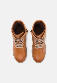 Bottines en cuir marron avec des lacets texturés, un bout arrondi et une doublure intérieure douillette. Elles possèdent une fermeture éclair sur le côté pour un accès facile.
