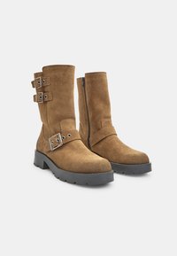 Pruunist kastanist keskpikkade varvastega saapad, millel on ümar varvas, hõbedased kinnitused, rihmad ja külgmine tõmblukk, paigutatud tekstuursele mustale tallale.