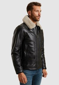 Črna usnjena jakna s krznjenim ovratnikom, zadrgo in dvema sprednjima žepoma. Ima gladko teksturo in prilegajoč kroj.