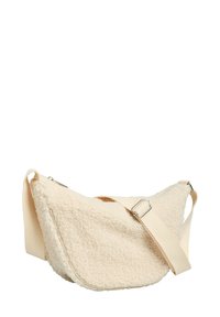 Bolso de piel sintética tipo borrego en color crema, con forma curva, correa ajustable de tela y un forro interior suave. Cuenta con detalles de herrajes metálicos.