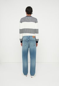 Καρό γκρι και λευκό πουλόβερ πλεκτό σε συνδυασμό με ξεθωριασμένα μπλε ίσια τζιν που έχουν δερμάτινη ραφή στην πλάτη και ελαφρύ φθορά.