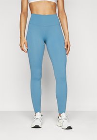 Leggings de un bleu deschis cu un talie înaltă, textură netedă și design ajustat; asortate cu pantofi atletici albi.