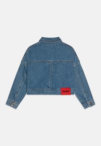 Lyseblå denim cropped jakke med et rødt "HUGO"-merke, lange ermer, knappe-mansjetter og sømdetaljer. Bakfra vises sømdetaljer.