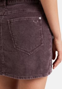 Paarse corduroy rok met een gestructureerd, ribbelpatroon. Voorzien van een ruitvormige achterzak met geborduurd hartlogo en een knoopdetail.