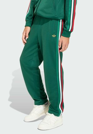 Zelené teplákové kalhoty s bílými, červenými a zelenými postranními pruhy. Na přední straně je zlaté logo. Tkanina je hladká a střih volný.