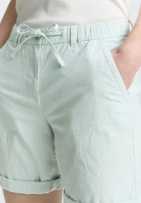 Shorts vert clair en tissu texturé avec des rayures verticales. Dotés d'une taille élastique avec cordon de serrage et de poches latérales.