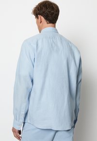 Lichtblauwe blouse met lange mouwen, gemaakt van gestructureerde stof, met een button-down kraag en knopen bij de manchetten.