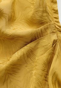 Gele stof met een textuurpatroon van palmbladeren, waarbij gouden borduursels diepte en ingewikkelde details aan het oppervlak toevoegen.