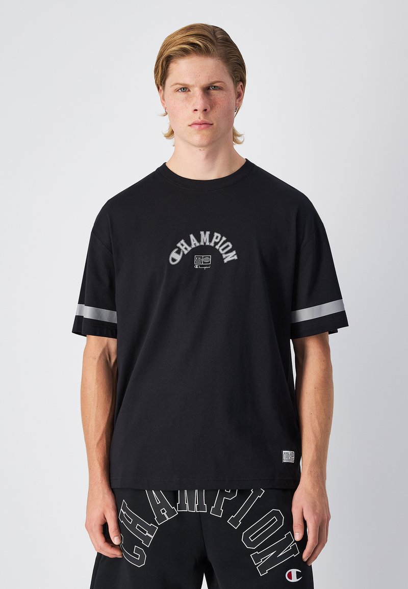 Camiseta de algodón negra con cuello redondo, corte holgado y acentos de rayas grises en las mangas. Logo de texto "Champion" en un diseño curvado en la parte delantera.