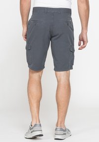 Pantaloni cargo grigi in tessuto, caratterizzati da molteplici tasche laterali e una vestibilità ampia, rifiniti con una texture liscia. Indossati con sneaker grigie.