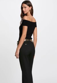 Top nero senza spalle con texture a costine, abbinato a pantaloni neri e una cintura con dettagli circolari in oro.